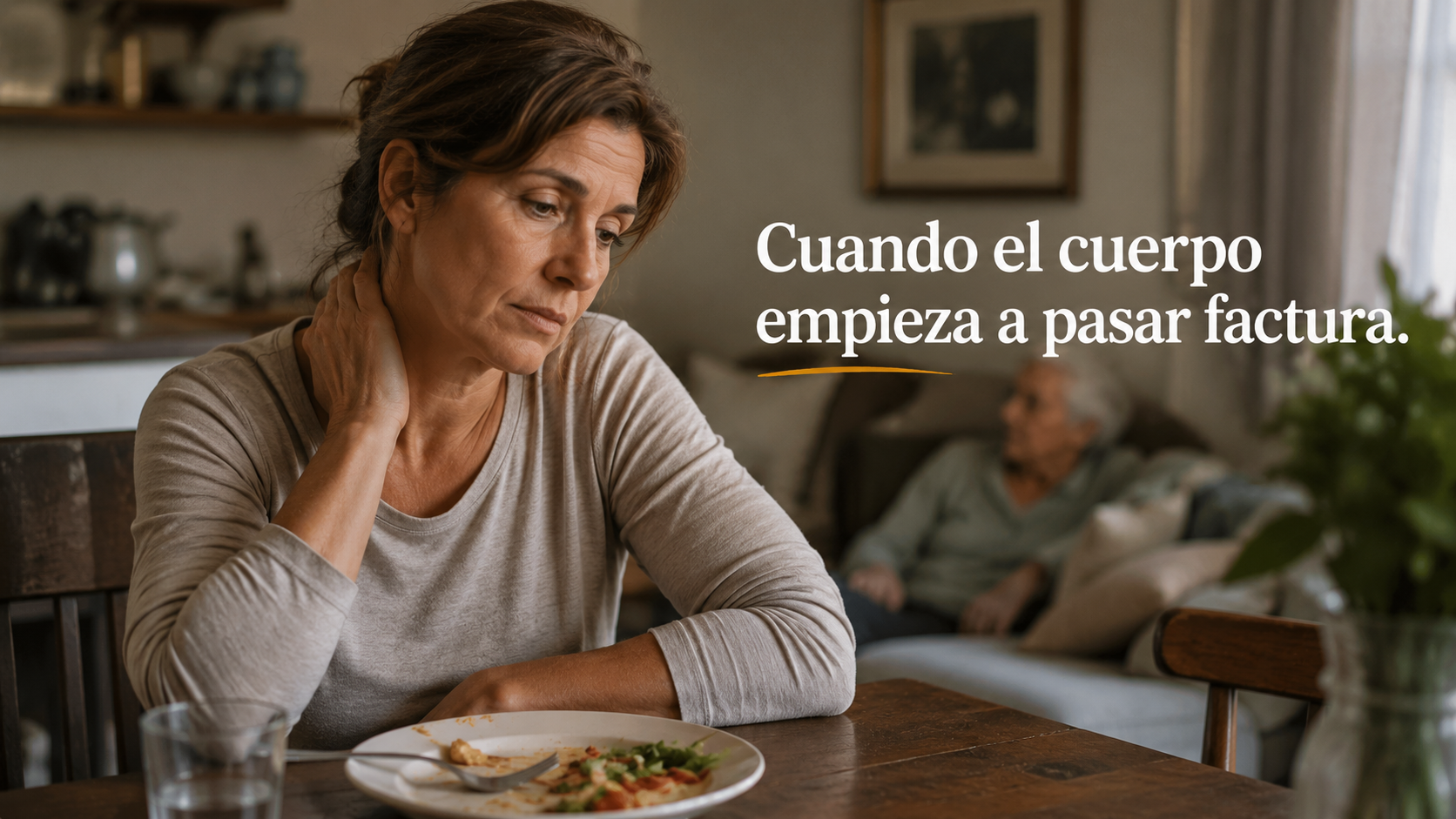 Cuidadora con dolor de cuello sentada a la mesa, con una persona mayor al fondo, ilustrando el agotamiento físico y emocional del cuidador familiar